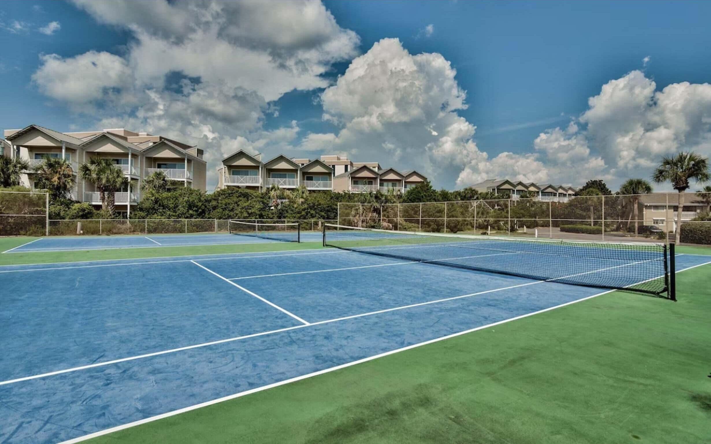 Un court de tennis avec un filet, entouré de verdure et de bâtiments.