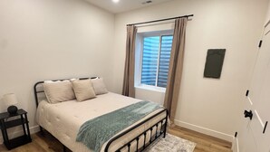 Une chambre à coucher avec un lit, une table de chevet, une fenêtre avec des rideaux et une porte.