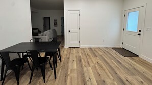 Une pièce comprenant une table à manger, des chaises, une porte et donnant sur une autre pièce.