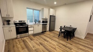 Une cuisine moderne avec un plancher en bois, des appareils électroménagers en acier inoxydable et un coin repas comprenant une table et des chaises.