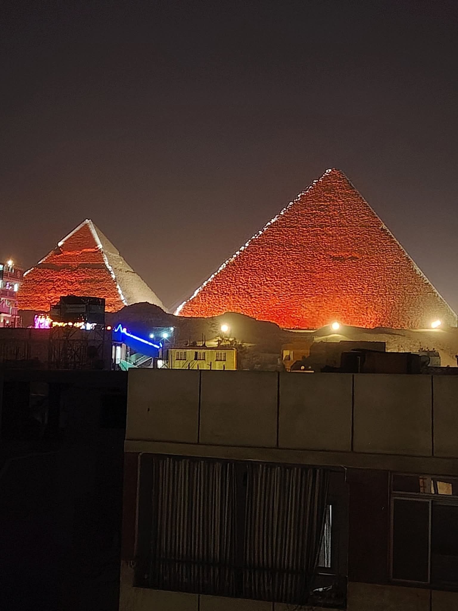 A large pyramid-shaped structure illuminated at night with a red hue.