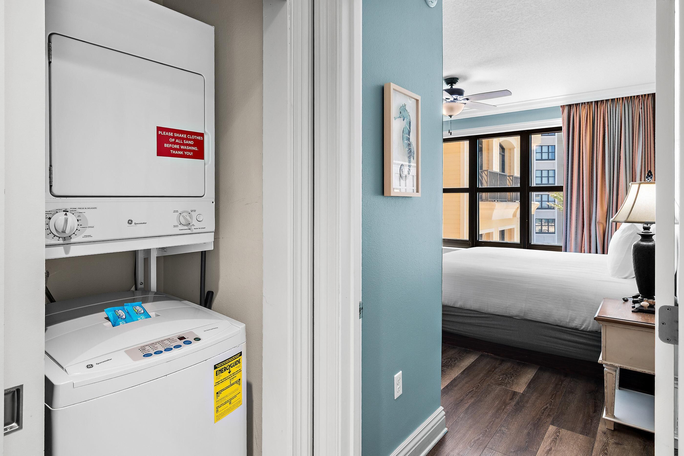 A hotel room with a bed, a window with curtains, a ceiling fan, and a washing machine.