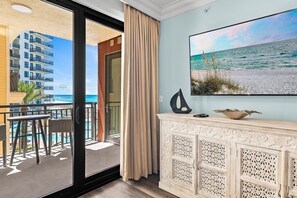 Ein Balkon mit Blick auf das Meer und ein Gebäude, ein weißer Konsolentisch mit dekorativen Schnitzereien und ein Strandbild.