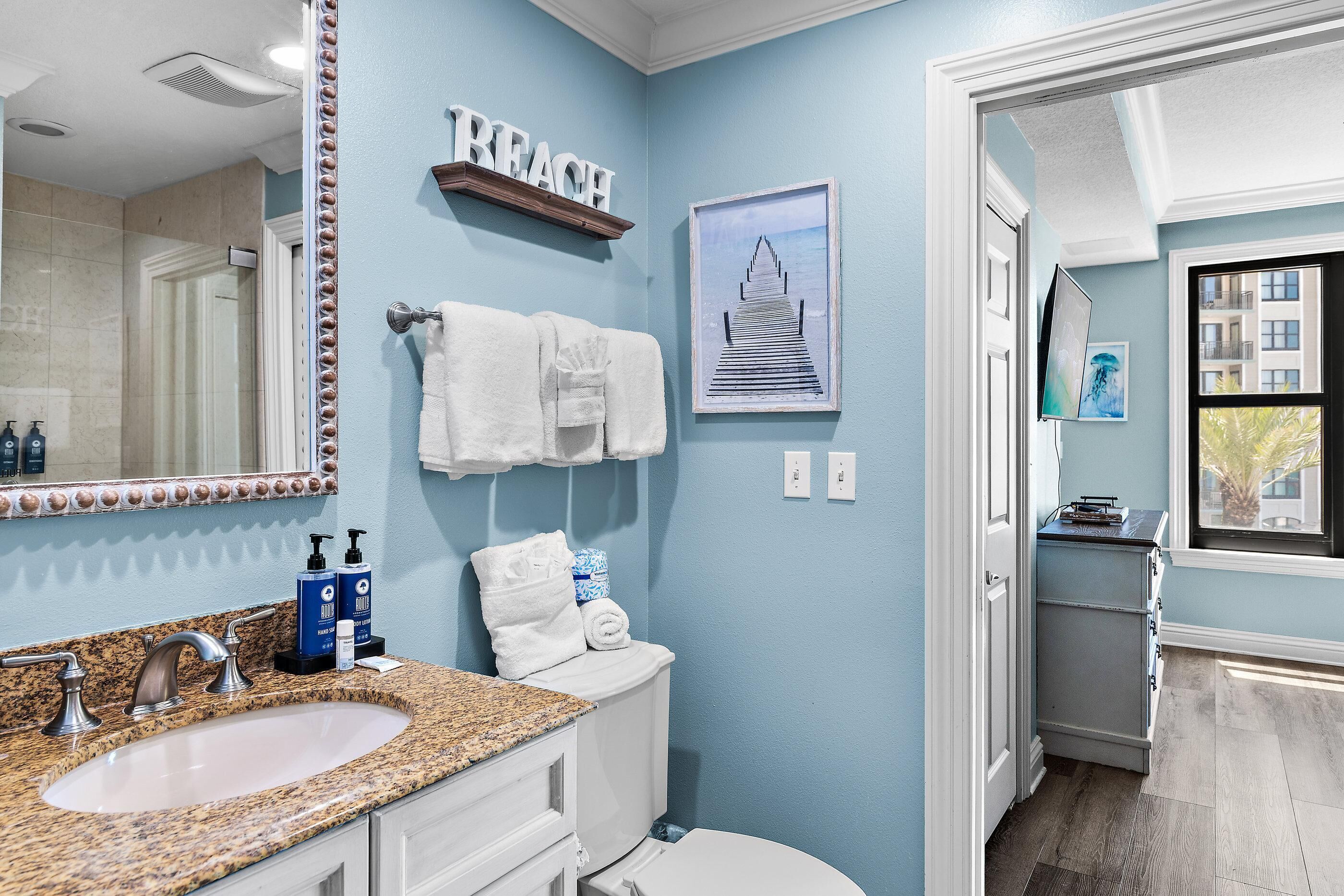 A bathroom with a granite countertop sink, a white toilet, a towel rack, and a framed picture of a pier.