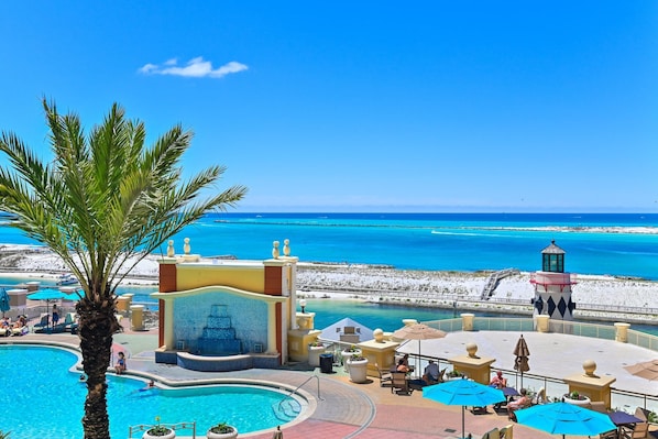 Poolbereich eines Resorts mit Palme, Wasserspiel und Blick auf den Strand.