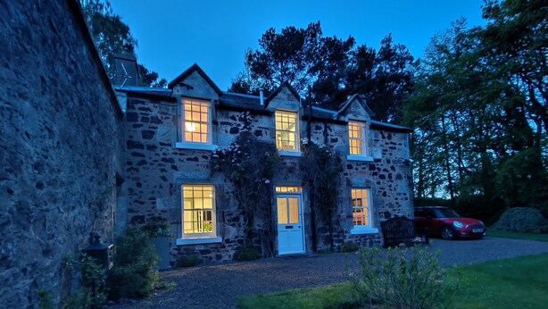 A stone building with multiple windows, a door, and a car parked outside.