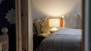 A bedroom with a bed, bedside table, lamp, and a vase of flowers.