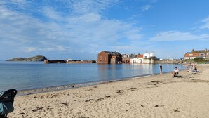 A sandy beach with a calm sea, a small island, and a row of buildings along the shore.