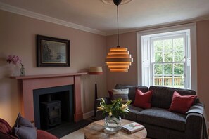 A living room with a fireplace, a sofa, a table with a vase, and a hanging light fixture.