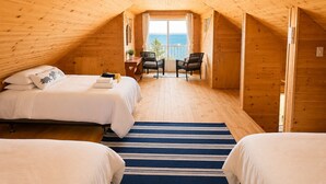 Ein Schlafzimmer einer Holzhütte mit zwei Betten, Blick auf das Meer und einem Balkon.