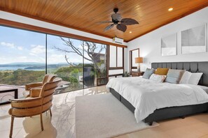 Ein Schlafzimmer mit einem großen Bett, einem Sessel, einem Deckenventilator und Blick ins Freie.