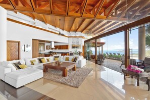 Ein geräumiger Wohnbereich mit weißem Sofa, Holztisch und Blick auf das Meer durch große Glasfenster.