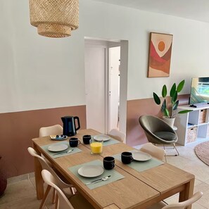 Ein Essbereich mit einem Holztisch, gedeckt für zwei Personen, einer Kaffeemaschine und einem Fernseher im Hintergrund.