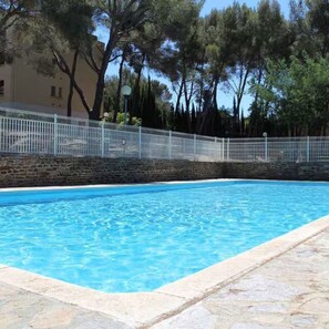 Ein rechteckiger Swimmingpool mit klarem, blauem Wasser, umgeben von einer Steindeck und einem weißen Zaun.