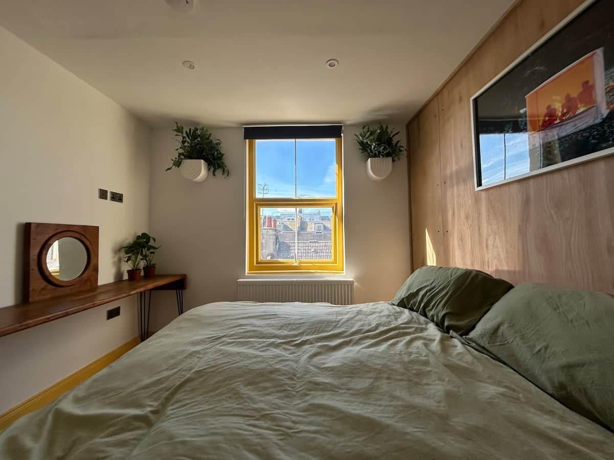 A bedroom with a bed, a window, a radiator, and two potted plants.