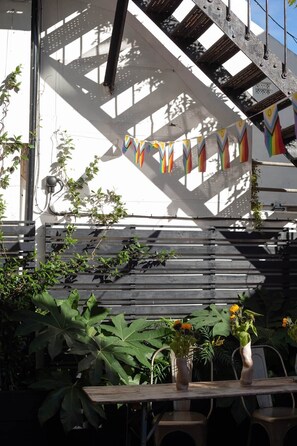 Un espacio al aire libre cubierto con un banco de madera, plantas en macetas y una barandilla metálica.