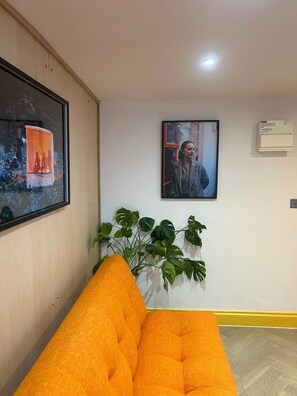 Una habitación con pared de madera, un cuadro enmarco, una planta en maceta y un sofá naranja brillante.