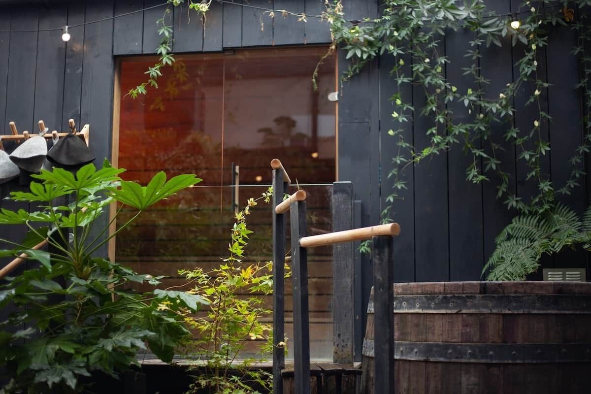A wooden deck with a hanging light fixture, a wooden barrel, and a large window with a view of a building.