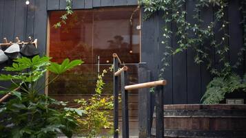 Una terraza de madera con una lámpara colgante, un barril de madera y un ventanal con vistas a un edificio.