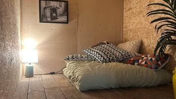 Un dormitorio acogedor en el ático con piso de madera, una cama con almohadas estampadas, un cuadro colgado en la pared y una lámpara.