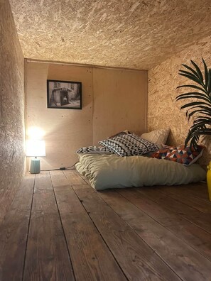 Un dormitorio acogedor en el ático con piso de madera, una cama con almohadas estampadas, un cuadro colgado en la pared y una lámpara.