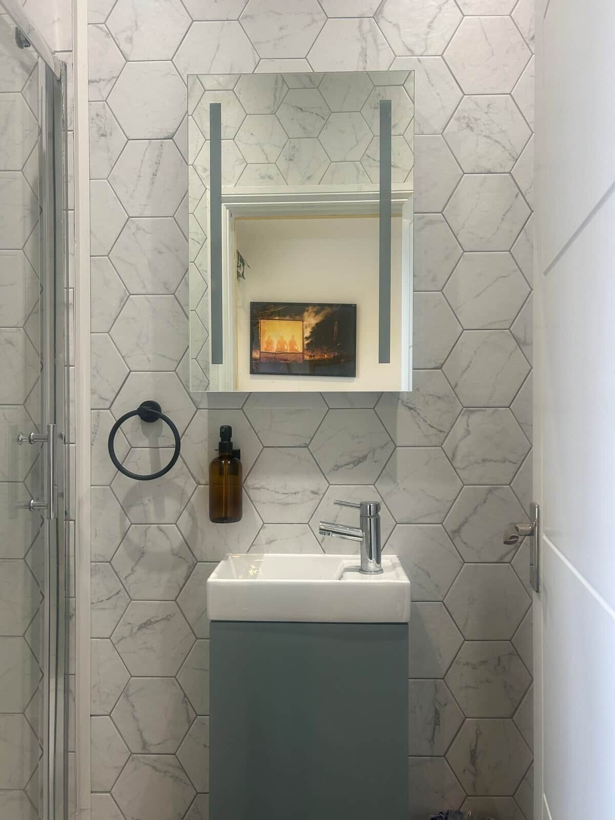 A bathroom with a hexagonal tile pattern, a rectangular sink with a modern faucet, a framed picture above the mirror, and a glass shower enclosure.