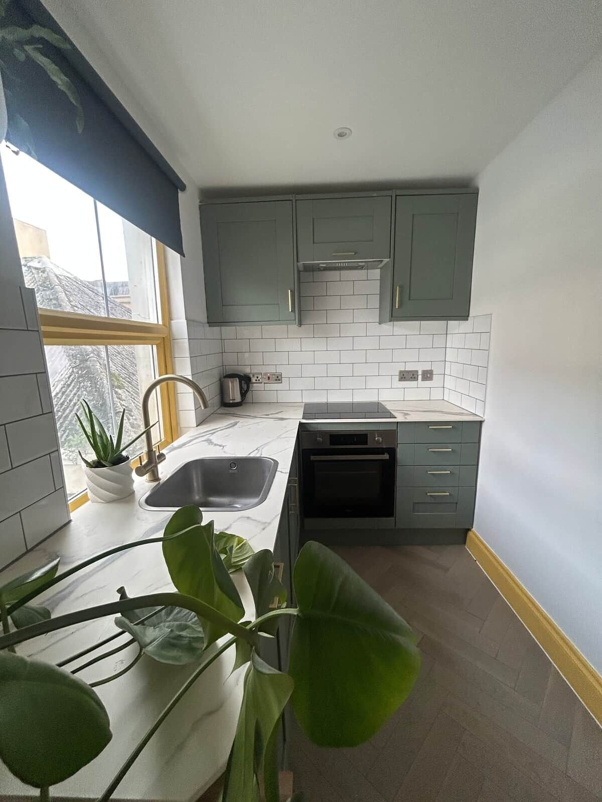 A kitchen with grey cabinets, white tiles, a sink, and an oven.