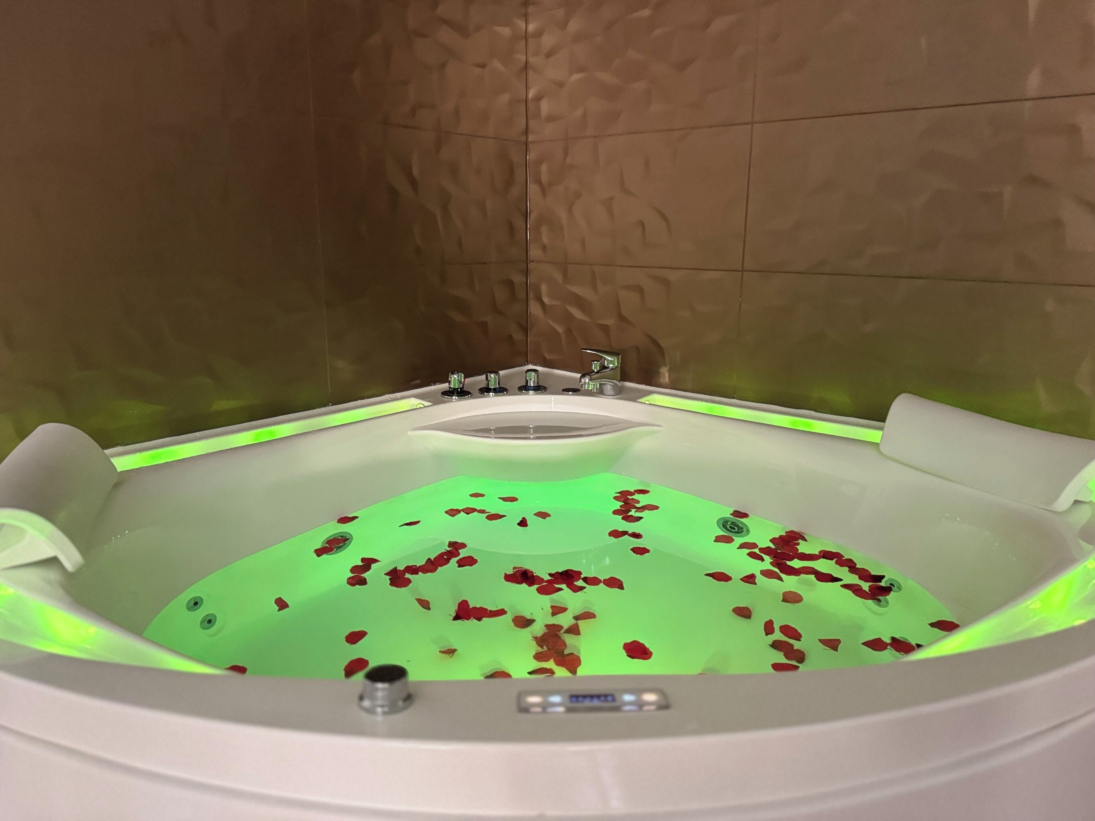 Una bañera con pétalos de rosa, una pantalla digital y una tira de luz verde.