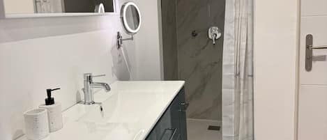 Un baño con lavamanos blanco, espejo y ducha.