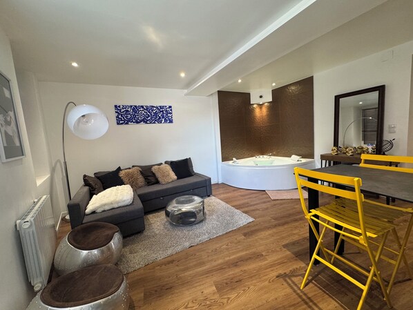 Un salon moderne avec un canapé, une table à manger entourée de chaises jaunes, un grand miroir et une baignoire.