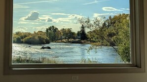 A framed view of a river with trees and a clear sky. - Henry`s Fork Suites Suite Two (Saint Anthony)
