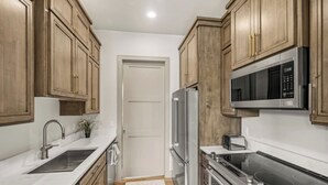A compact kitchen with wooden cabinets, a stainless steel refrigerator, a microwave, a toaster, and a sink. - Henry`s Fork Suites Suite Two (Saint Anthony)