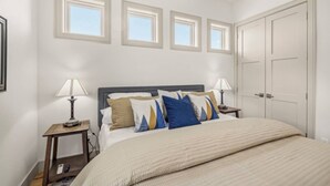 A bedroom with a bed, two bedside tables, a nightstand, and three windows. - Henry`s Fork Suites Suite Two (Saint Anthony)