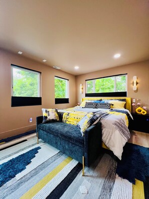 Une chambre à coucher comprenant un lit, une table de chevet, une commode, une fenêtre et un luminaire fixé au mur.