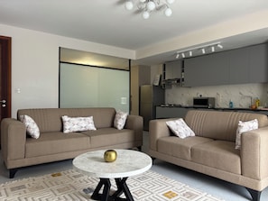 Ein modernes Wohnzimmer mit zwei Sofas, einem runden Couchtisch und einer Küche im Hintergrund.
