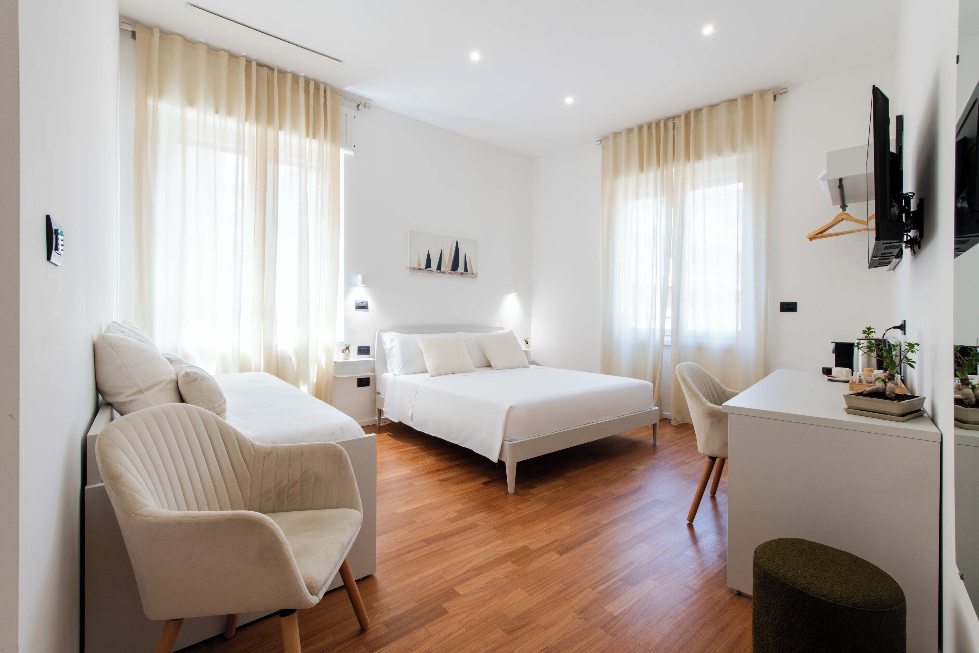 A modern hotel room with a bed, two chairs, a desk, and a TV.