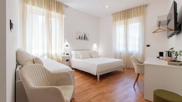 A modern hotel room with a bed, two chairs, a desk, and a TV.
