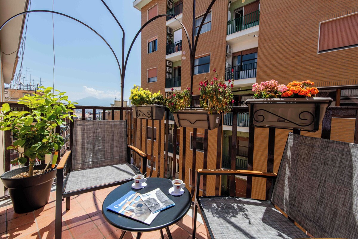 Un balcón con mobiliario exterior, una planta en maceta y un arreglo floral.