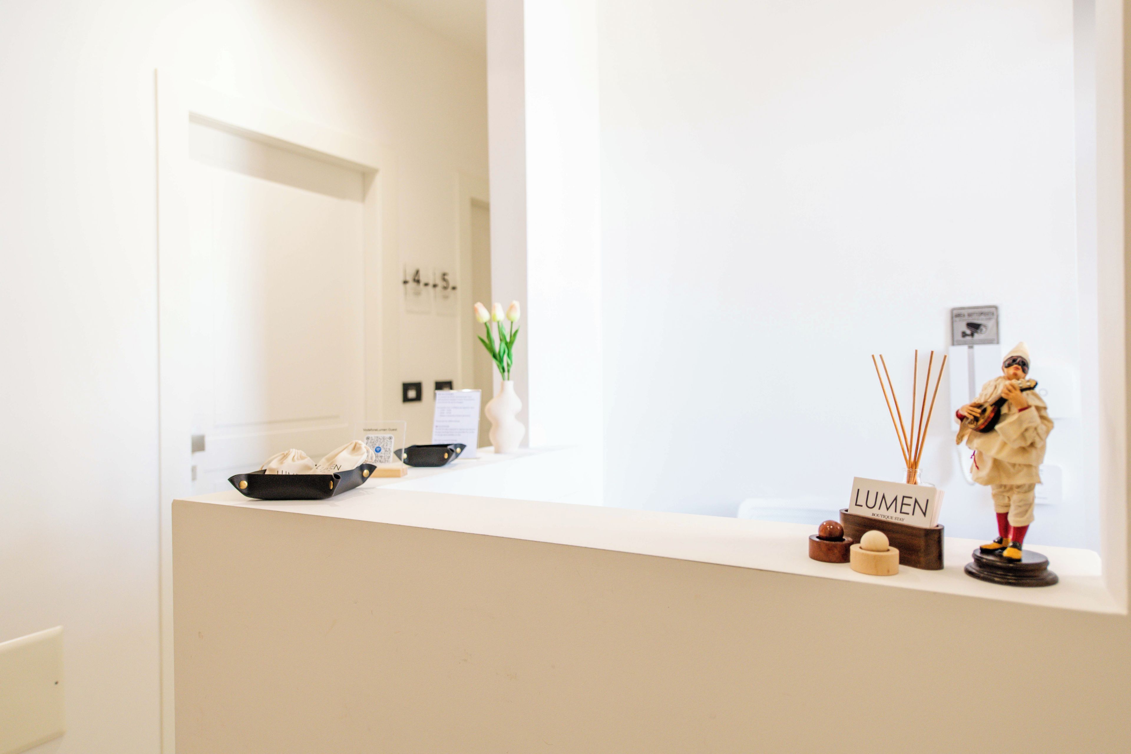 A reception desk with a vase of flowers, a small figurine, and a sign that reads 'LUMEN BOUTIQUE STAY'.