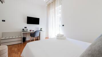 A hotel room with a bed, a desk with a chair, a television mounted on the wall, and a window with curtains.