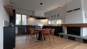 A modern kitchen with a dining area, large windows, and a fireplace. - THE HOUSE OF THE WOLF 2 | A shelter surrounded by nature (Colico)