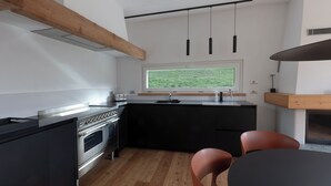 A modern kitchen with a large stove, a window with a view, and a dining area with chairs. - THE HOUSE OF THE WOLF 2 | A shelter surrounded by nature (Colico)