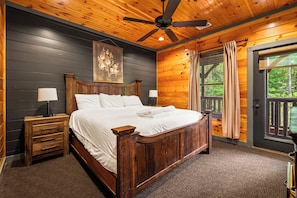 Quarto de madeira com cama, mesas de cabeceira, ventilador de teto e janela com cortinas.
