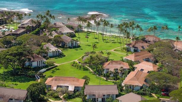 An aerial view of a coastal resort with multiple buildings, a well-maintained lawn, and a beach with palm trees. - Kiahuna 183 AC, Ground Floor Ocean View PBAC (Koloa)