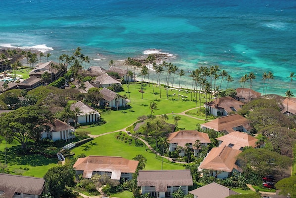 An aerial view of a coastal resort with multiple buildings, a well-maintained lawn, and a beach with palm trees. - Kiahuna 183 Ground Floor Ocean View PBAC (Koloa)