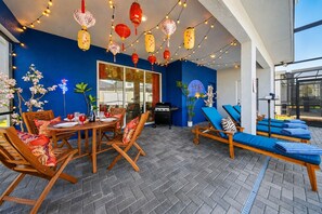 An outdoor patio area with a dining table, chairs, and lounge chairs. - Themed 6BR Cinematic Cove w Private Pool & Theater (Davenport)