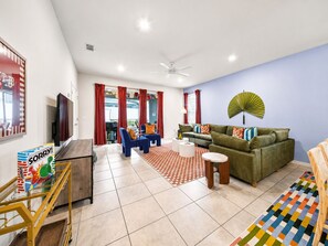 Een woonkamer met een bank, stoelen, een televisie en een ventilator.