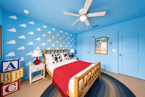 A child's room with a bed, a nightstand, a red lamp, alphabet blocks, a ceiling fan, and a door. - Themed 6BR Cinematic Cove w Private Pool & Theater (Davenport)