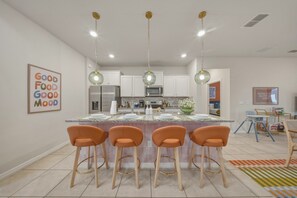 Eine moderne Küche mit einer zentralen Kochinsel, Barhocker, Pendelleuchten und einer Kücheninsel mit Mikrowelle und Kühlschrank.