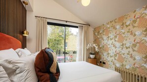 Ein Hotelzimmer mit Bett, einem Fenster mit Vorhängen, einem Heizkörper und einer Wand mit Blumenmuster.